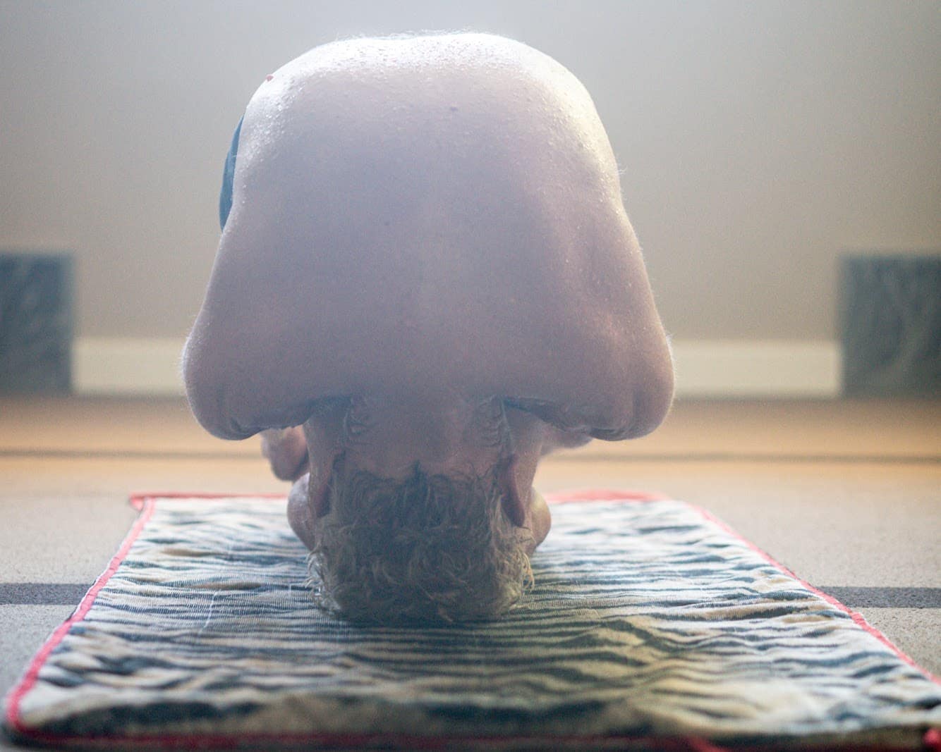 A practitioner inverted in a headstand, backlit through haze in the heated room.