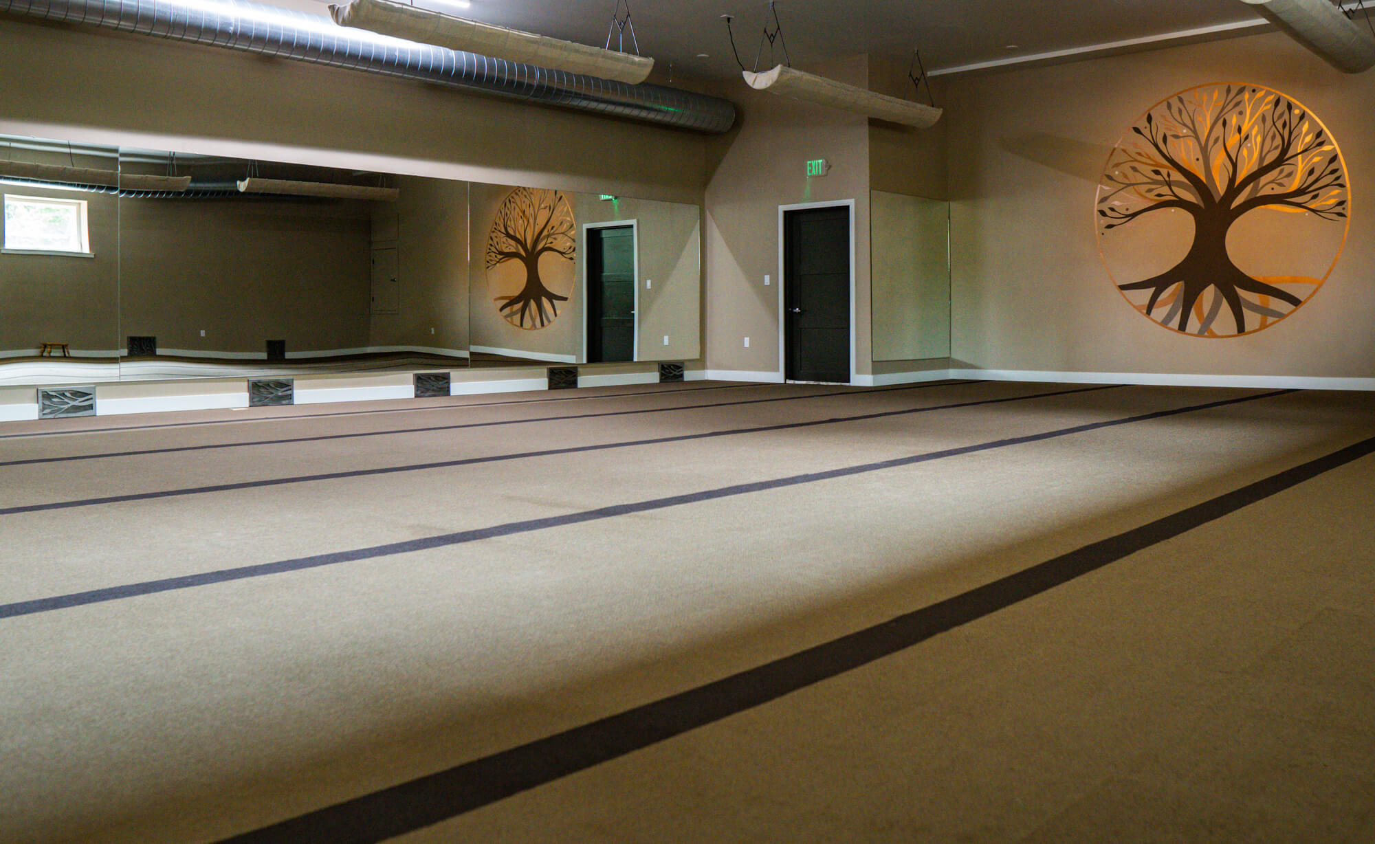 The empty practice room — warm walls, mirrors, and two large copper tree-of-life murals painted in circles.
